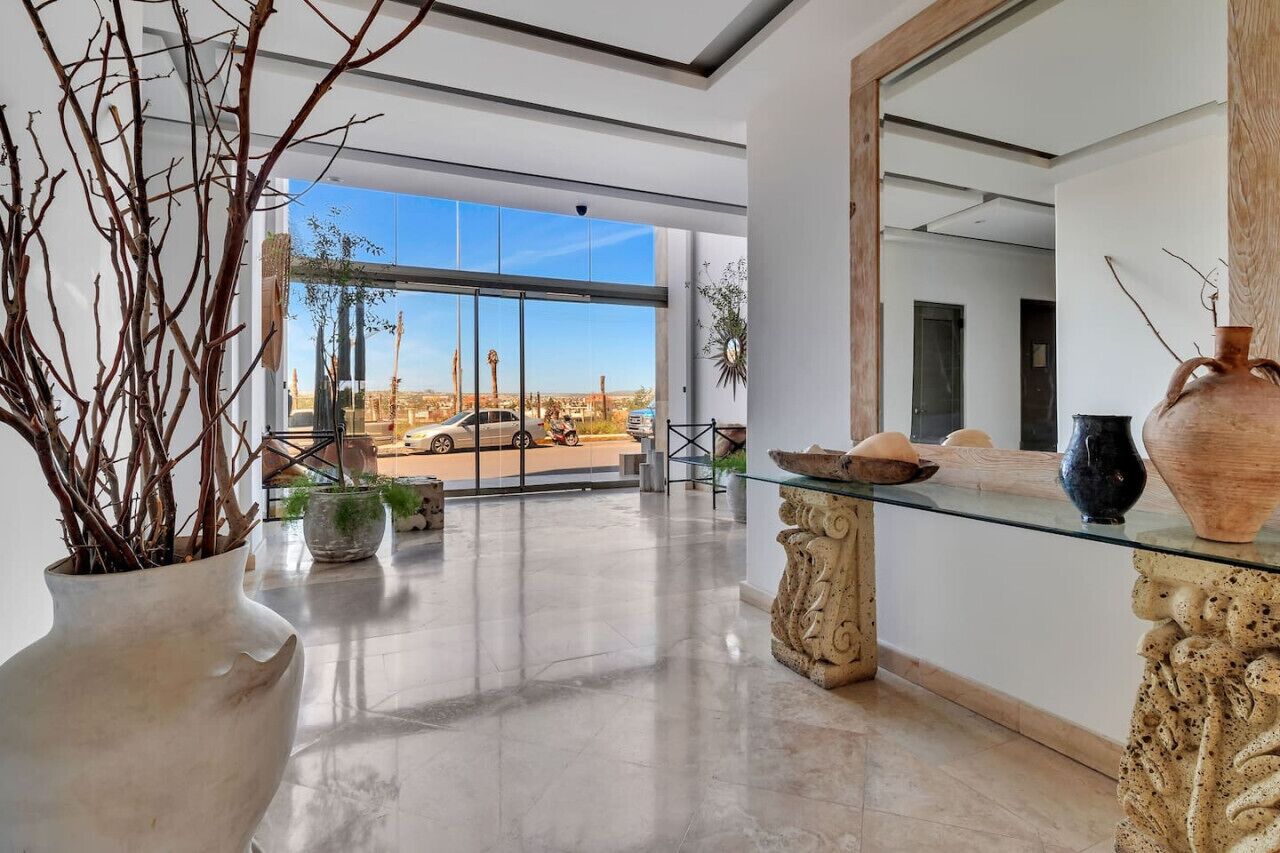 A spacious lobby with a large glass door leading to an outdoor area, a glass coffee table, and a large vase.