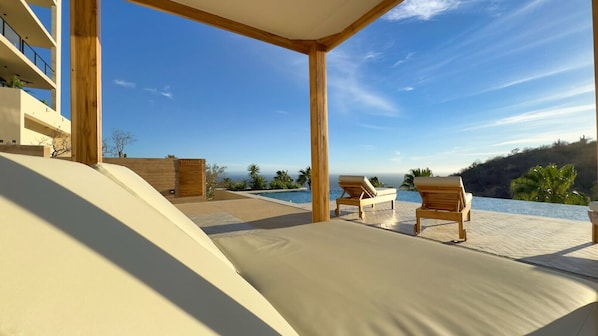 A poolside area with lounge chairs, a wooden pergola, and a view of the ocean.