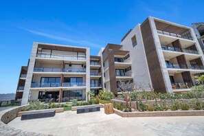 Een modern appartementencomplex met meerdere verdiepingen, balkons, een aangelegde tuin en een helder uitzicht op de omgeving.