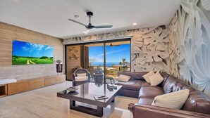 A modern living room with a large flat-screen TV, a ceiling fan, a brown leather sofa, and a glass coffee table. - Ocean View, Overlooking Quivira, Infinity Pool (Cabo San Lucas)