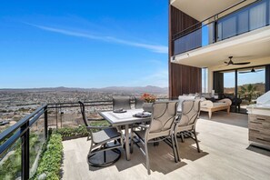 Een balkon met een eettafel en stoelen, een bank en een barbecueplek.