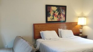 Habitación de hotel con dos camas, un cabecero de madera, un cuadro en la pared, una mesita de noche con una lámpara y una silla.