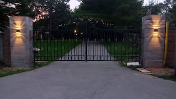 A gated driveway leading to a property with a paved path and a metal gate.