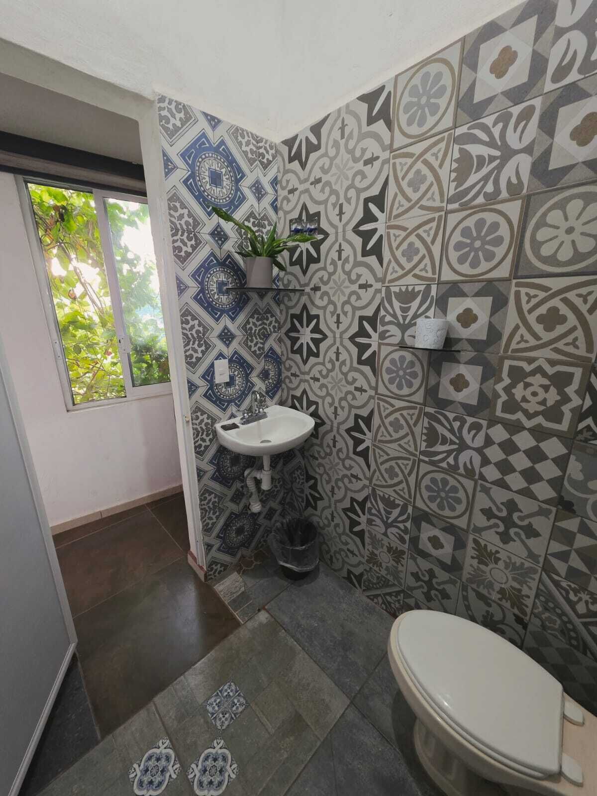 A bathroom with patterned tiles, a white sink, a toilet, and a window with greenery outside.