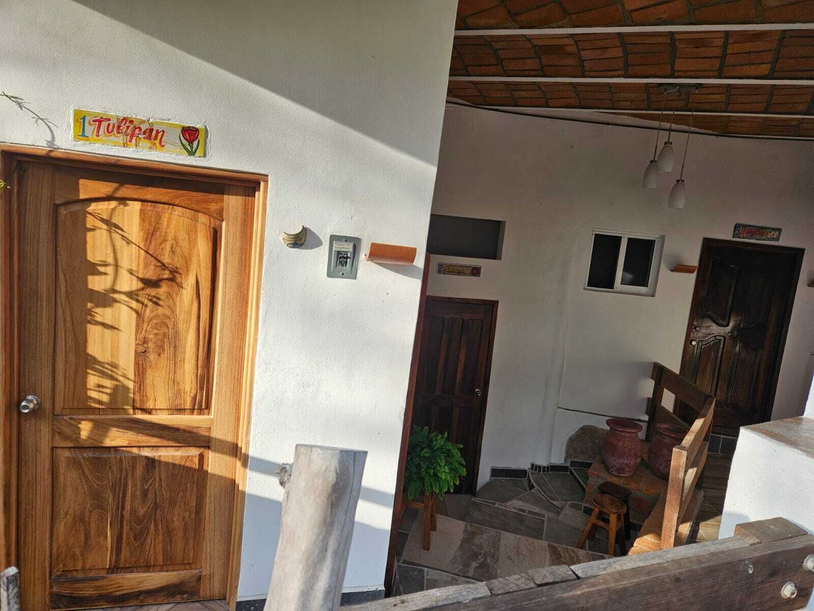 A wooden door with a sign above it, a small window, and a staircase leading to a room with a potted plant and a wooden bench.