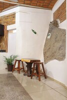 Una habitación con piso de baldosas, un banco de madera, una planta en maceta y una pared de ladrillo con una sección irregular.