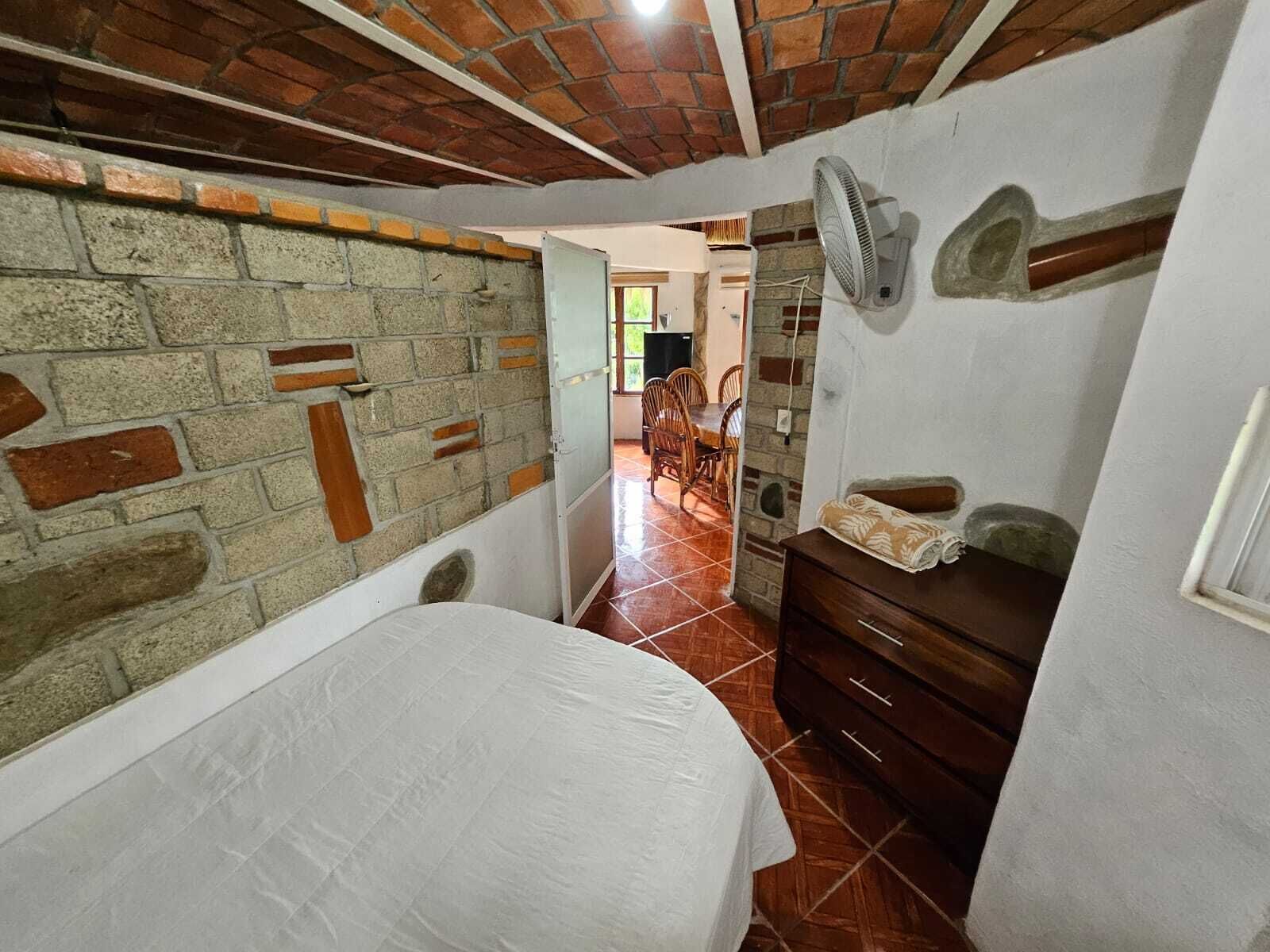 Un dormitorio con pared de ladrillo, cama, cómoda y ventilador.