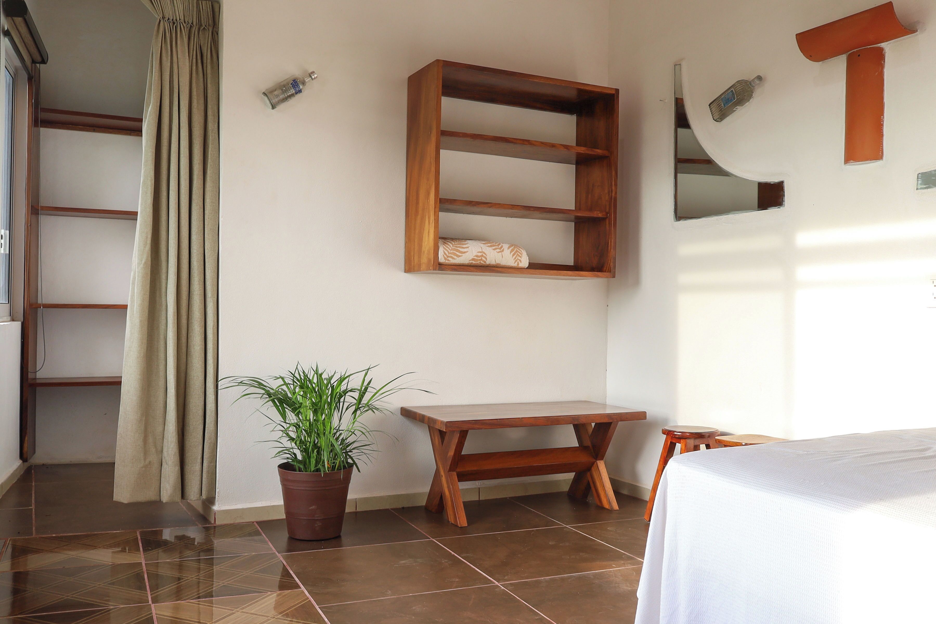A room with a wooden shelf, a potted plant, a wooden table, and a bed.