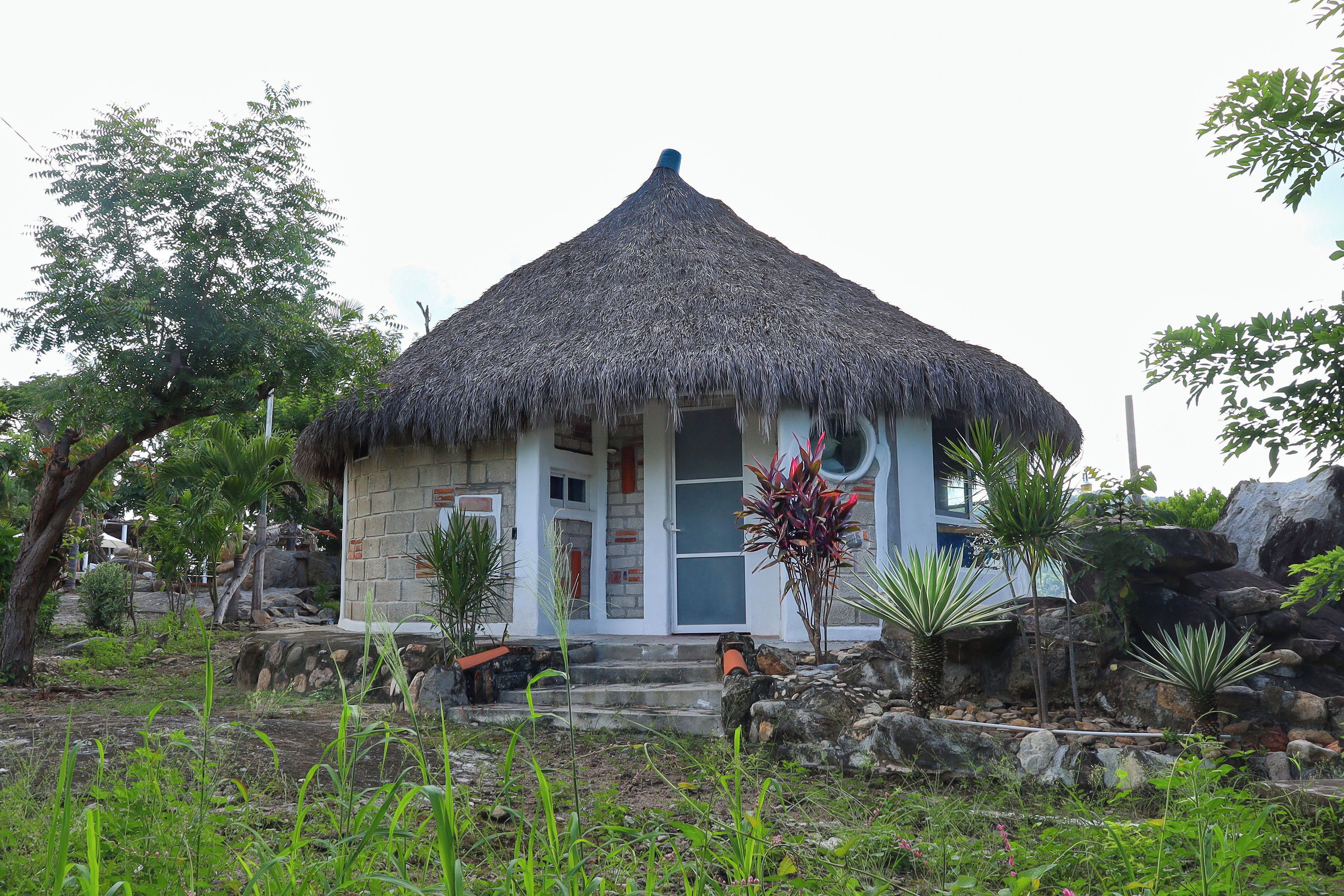 A small, thatched-roof building with a stone facade, surrounded by tropical vegetation and a rocky landscape.