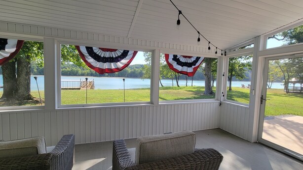 Une terrasse couverte, meublée de meubles en osier, dotée de grandes fenêtres et décorée de drapeaux américains.