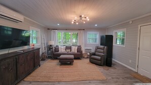 A living room with a TV, sofa, and chairs, large windows, and a ceiling fan. - 20% Off Lakefront Tiny Bird Dock, Hot Tub, Firepit, Boat House, ParkLike Setting (Dandridge)