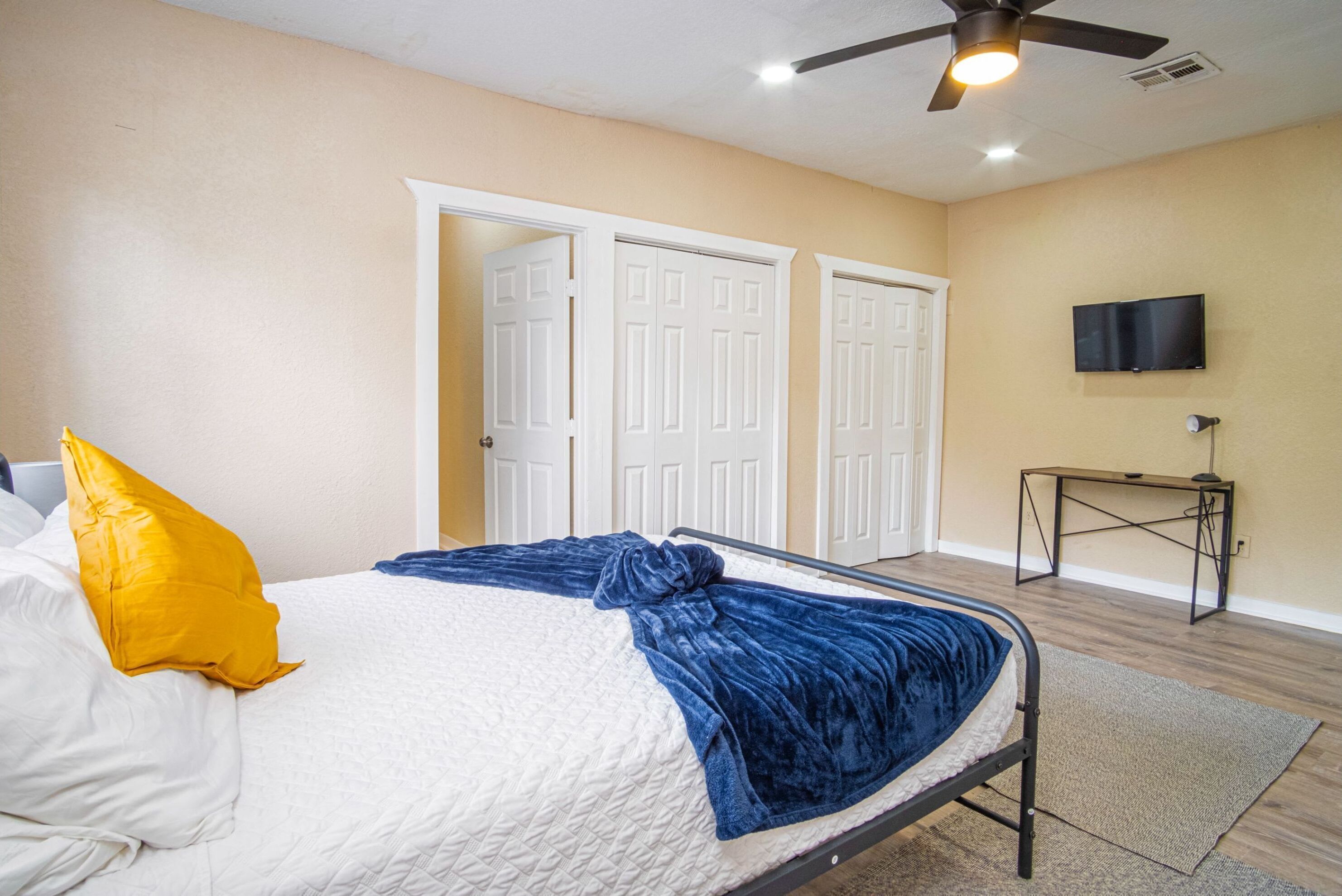 A bedroom with a bed, a ceiling fan, a TV, and a desk.