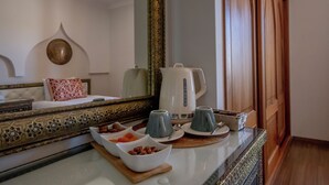 A hotel room with a bed, a bedside table with a kettle, cups, and bowls of fruit. - Al Karob Yoga Boutique Hotel (Albufeira)