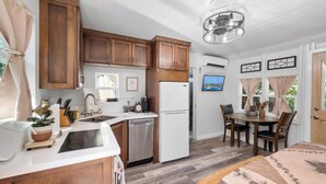 A compact kitchen with wooden cabinets, a white refrigerator, and a dining area with a table and chairs. - Julian Cafe Couples Cottage - Breakfast Included at The Julian Cafe & Bakery! (Julian)