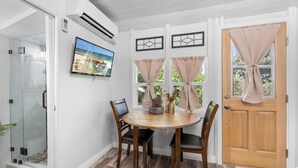 A dining area with a round table, four chairs, a television on the wall, and a wooden door with curtains. - Julian Cafe Couples Cottage - Breakfast Included at The Julian Cafe & Bakery! (Julian)