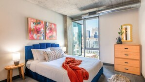 Een moderne slaapkamer met een groot bed, uitzicht over de stad en een dressoir met lades.