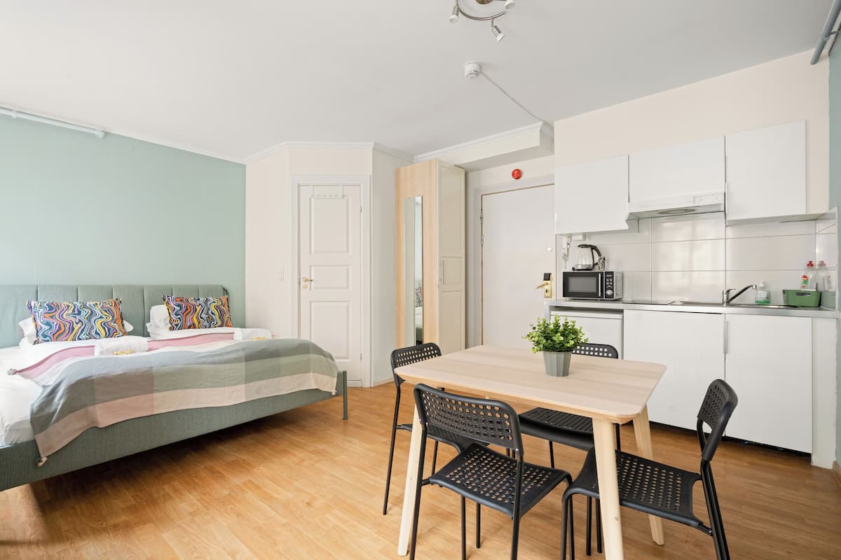 Un espace de vie compact comprenant un lit, une table à manger avec des chaises, un petit coin cuisine et une porte donnant sur une autre pièce.