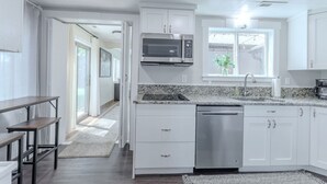 A modern kitchen with white cabinets, a stainless steel dishwasher, a built-in microwave, and a window with a view. - Courtyard Hot Tub in the Heart of Downtown (Panguitch)