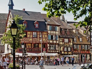 A traditional European street with half-timbered buildings, outdoor seating, and a clear sky. - Ancien Relais 2 Clim/A-C (Colmar)