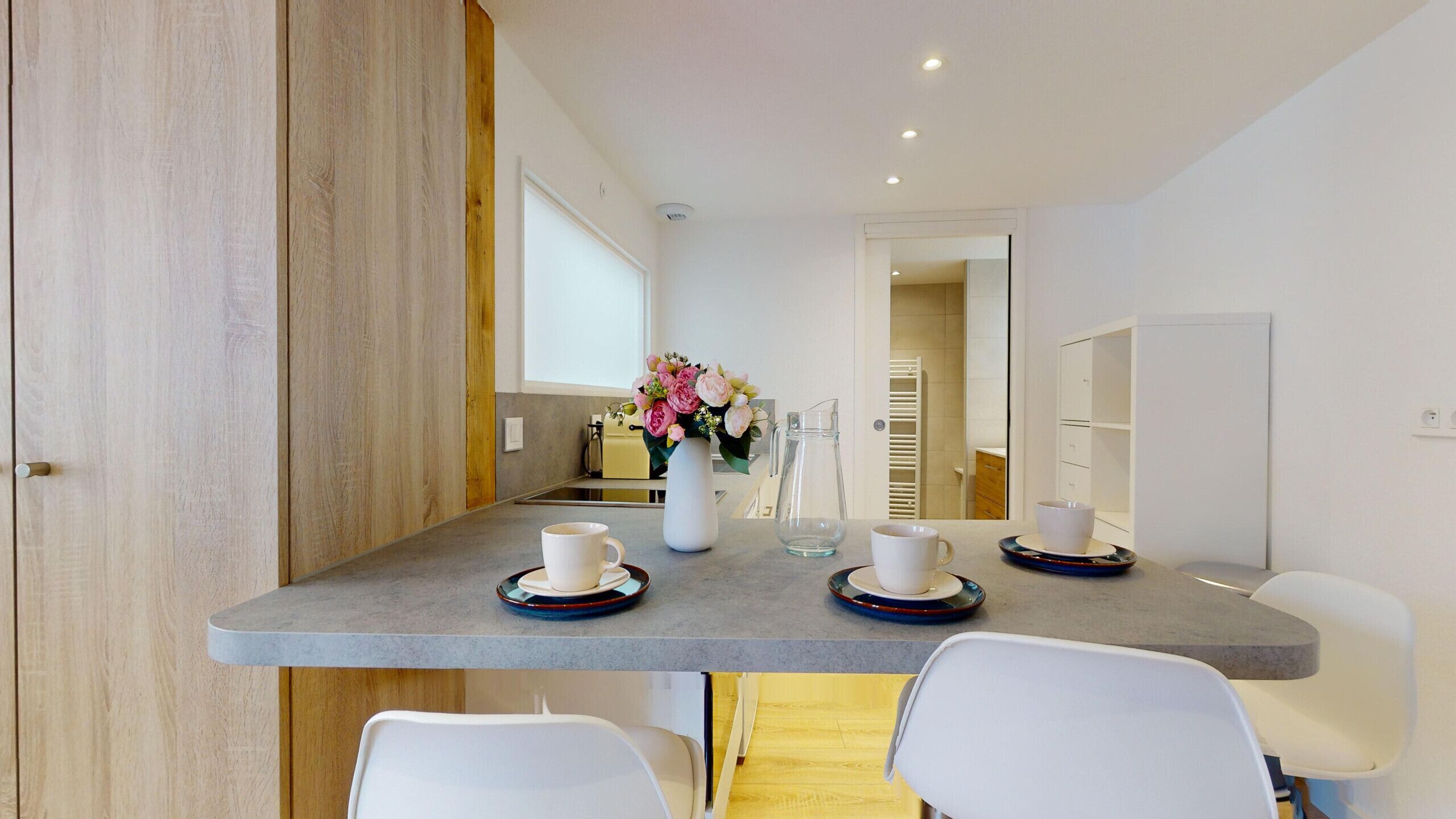 Un espace repas moderne avec une table grise, des chaises blanches et un vase rempli de fleurs.
