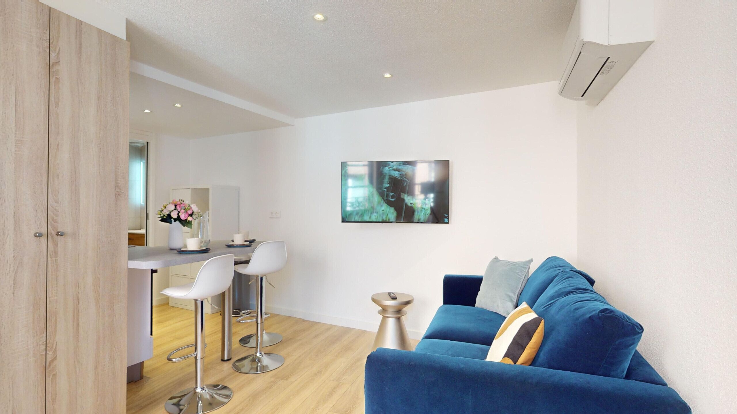 Un salon moderne avec un canapé bleu, des chaises blanches et un coin cuisine à l’arrière-plan.