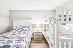 A bedroom with a bed, a nightstand, a lamp, and two bunk beds. - Beach Cottages Ocean View Condo (Indian Shores)