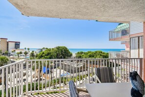 A balcony with a view of the beach and ocean, a chair, and a table.