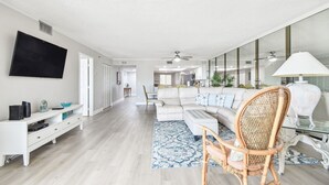 Un salon moderne avec un canapé d’angle, un téléviseur et un coin repas à l’arrière-plan.