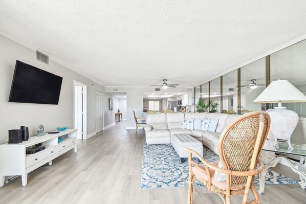 A modern living room with a sectional sofa, a television, and a dining area in the background. - Beach Cottages Ocean View Condo (Indian Shores)