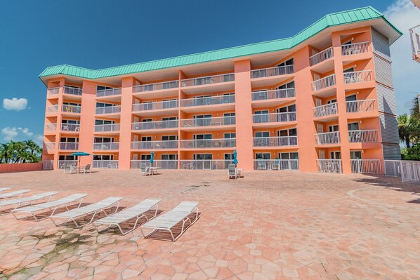 A multi-story hotel with balconies, a tiled courtyard, and lounge chairs.