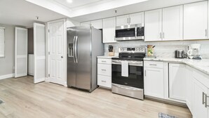 Une cuisine moderne avec des armoires blanches, des appareils en acier inoxydable et un plancher en bois.