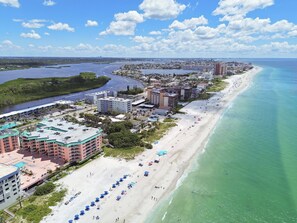 A coastal cityscape with a wide beach, clear blue waters, and a mix of residential and commercial buildings. - Beach Cottages Ocean View Condo (Indian Shores)