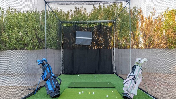 Ein Golf-Übungsbereich mit Netzabdeckung, Abschlag und Putting-Matte.