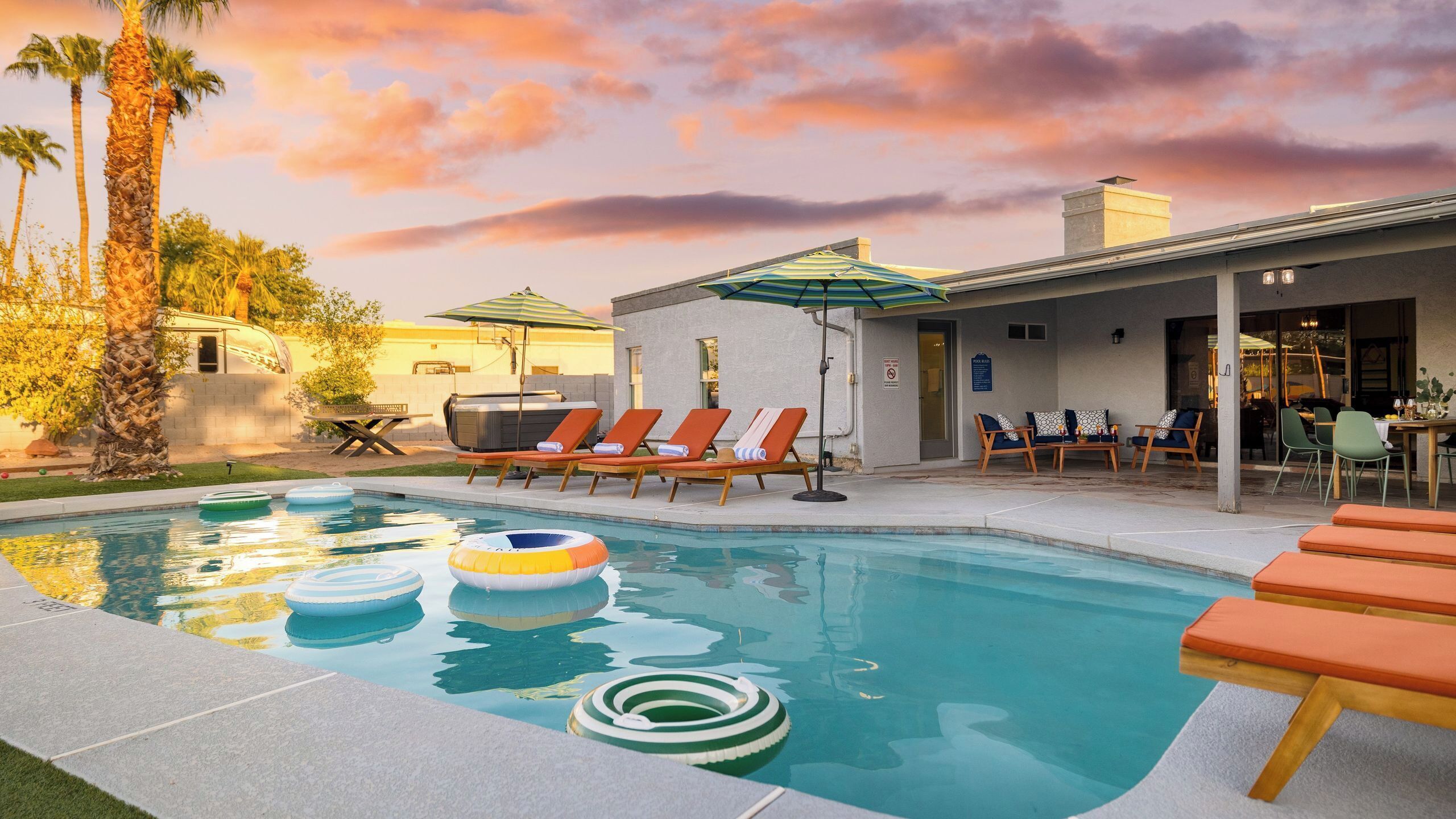 A pool area with lounge chairs, a hot tub, and a covered patio with outdoor seating.