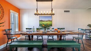 A dining area with a long table, chairs, a hanging light fixture, and a large window with blinds. - Fairway Oasis by Avantstay Ultimate Scottsdale Oasis! (Scottsdale)