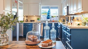 A kitchen with a wooden table, a glass vase with flowers, a glass dome over a muffin, and two glass bottles. - Fairway Oasis by Avantstay Ultimate Scottsdale Oasis! (Scottsdale)