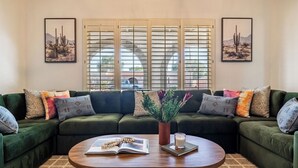 A living room with a green sectional sofa, a coffee table, and two windows with blinds. - Fairway Oasis by Avantstay Ultimate Scottsdale Oasis! (Scottsdale)