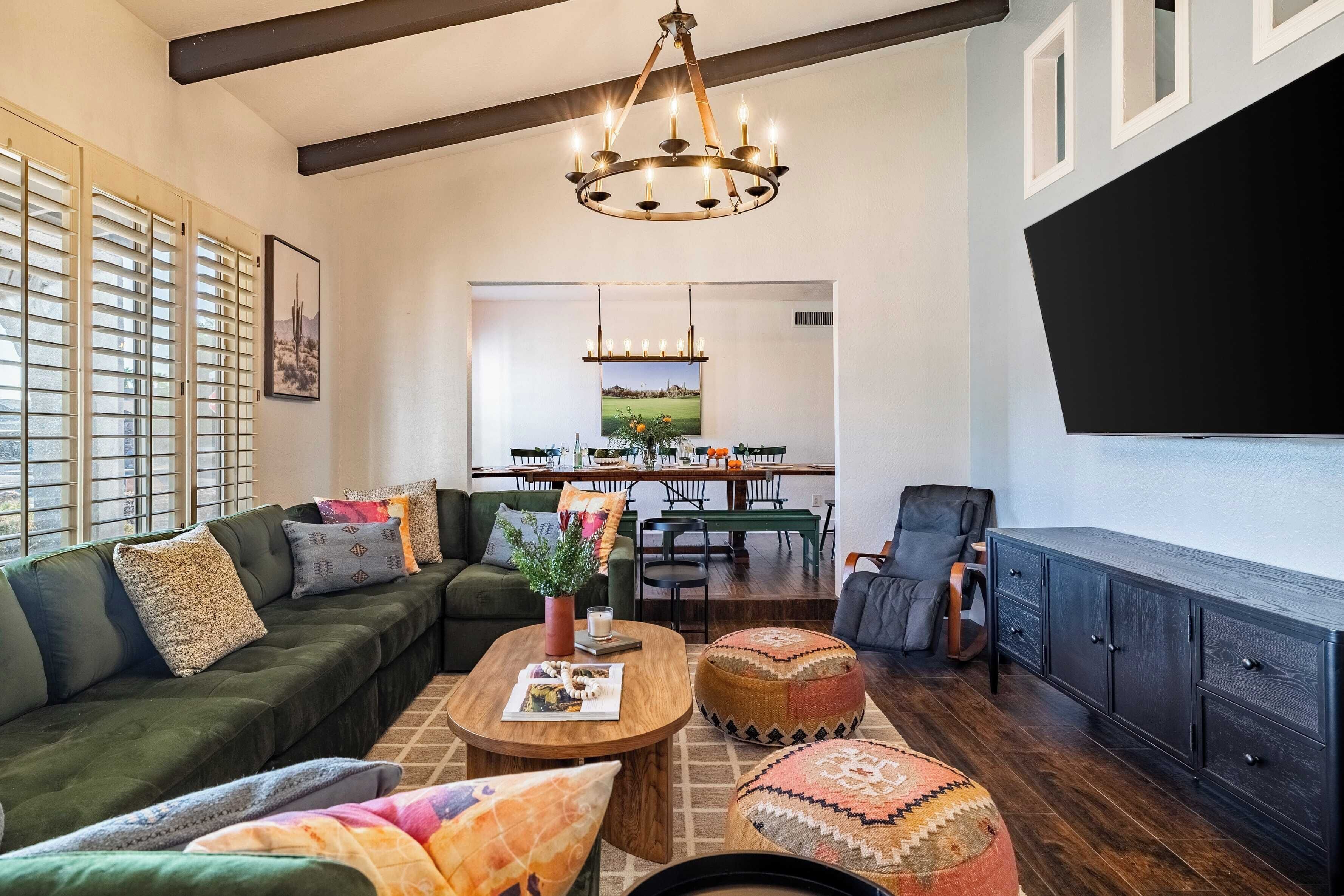 A spacious living room with a sectional sofa, a coffee table, ottomans, a dark wooden cabinet, and a dining area with a table and chairs.