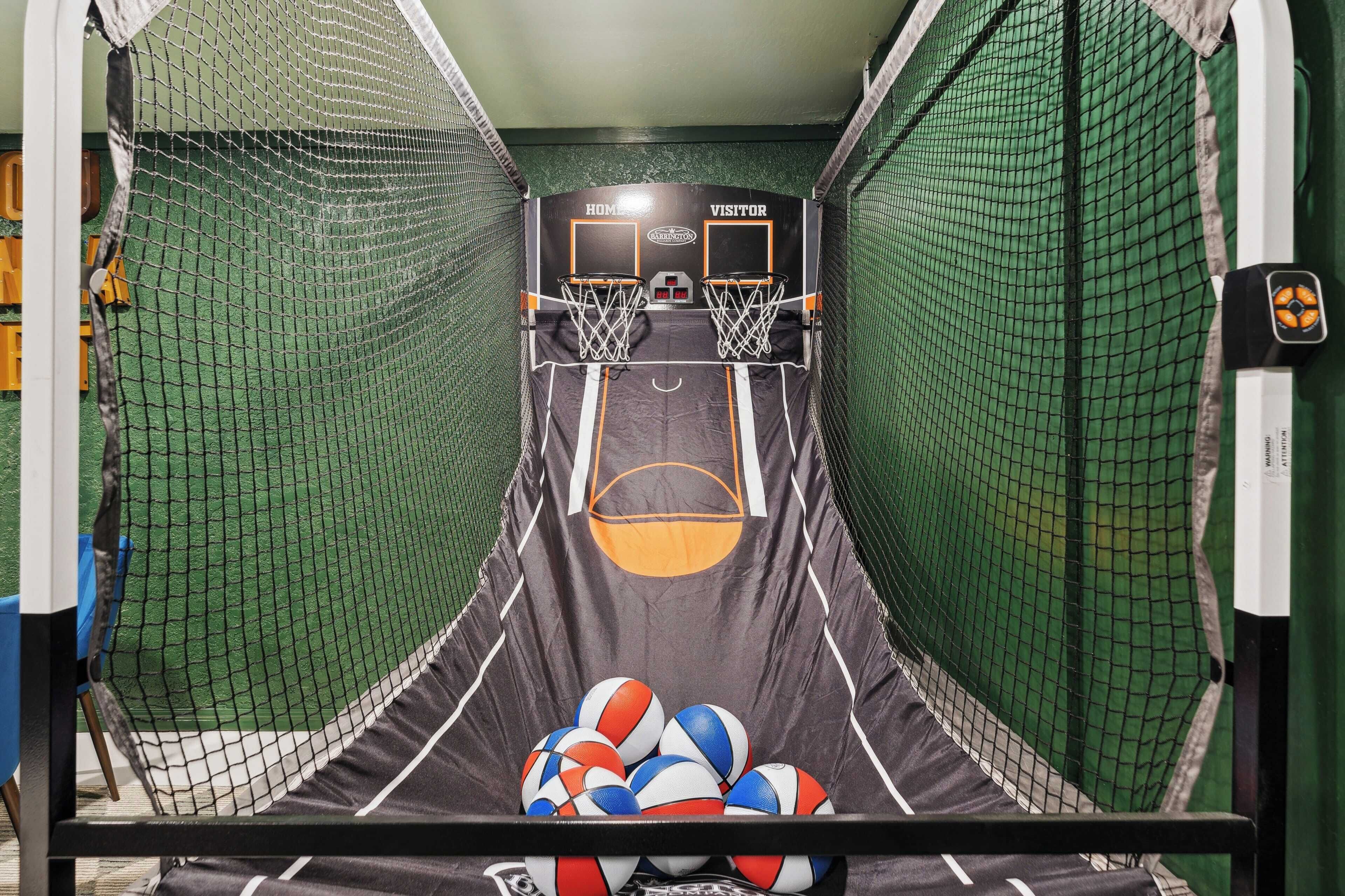 Un terrain de basket avec deux paniers, l’un portant l’inscription « ÉQUIPE RÉSIDENTE » et l’autre « ÉQUIPE VISITEUSE », et une pile de ballons de basket près de la ligne des lancers francs.