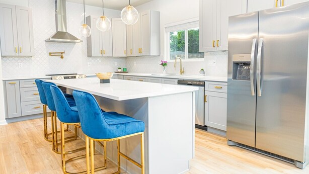 Una cocina moderna con armarios blancos, un refrigerador de acero inoxidable, una isla central con taburetes azules e iluminación colgante.