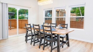 Un comedor con mesa y sillas de madera, ventanas amplias y vista a una terraza de madera.