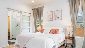 Un dormitorio con cama, mesita de noche, lámpara y puerta que da a un baño.