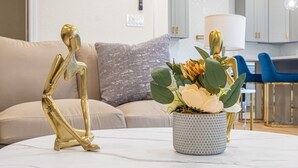 Una sala de estar moderna con un sofá, una figura dorada decorativa y un florero con flores sobre una mesa de mármol.