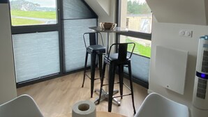 A modern room with a dining table, two chairs, a large window, and a ceiling light fixture. - Renovated house with panoramic view of the bay and the 7 islands  (Perros-Guirec)