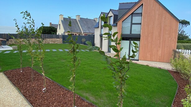 A modern building with a sloped roof and large windows, surrounded by a well-maintained lawn and young trees. - Renovated house with panoramic view of the bay and the 7 islands  (Perros-Guirec)