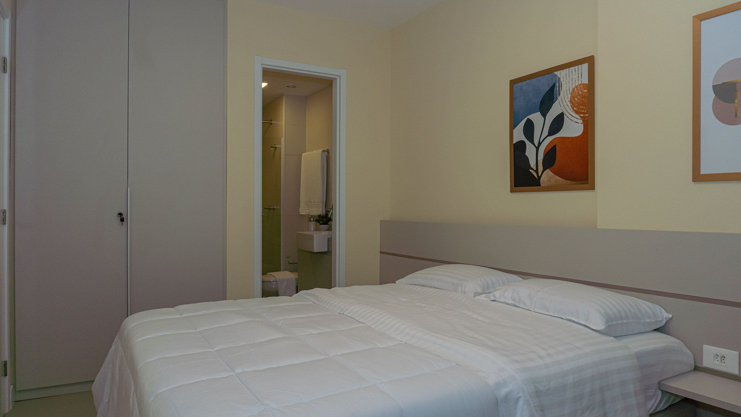 A hotel room with a bed, a bathroom visible through an open door, and a painting on the wall.