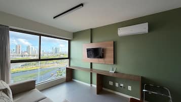 Ein modernes Zimmer mit großem Fenster, einem Flachbildfernseher an einer Holzkonsole und Blick auf die Stadt.