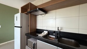 A compact kitchen with a refrigerator, stove, sink, and wooden cabinets. - Flats no Parque Shopping por Yolo (Recife)