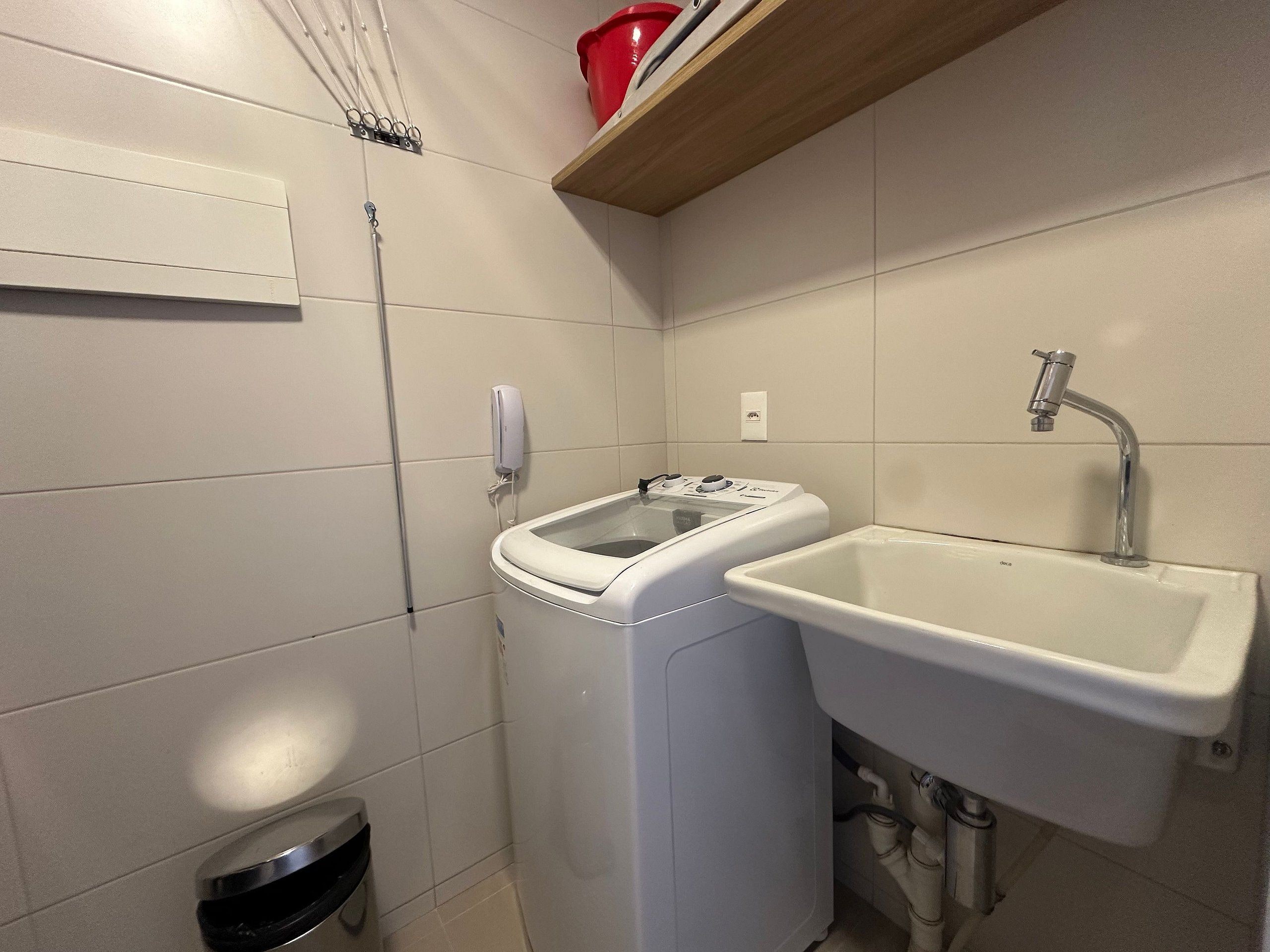 Un baño pequeño con lavadora, lavamanos y un cubo de basura.