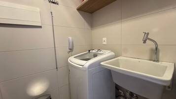 Un baño pequeño con lavadora, lavamanos y un cubo de basura.